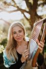 Mulher encantadora romântica com cabelo loiro apreciando melodia enquanto toca instrumento musical e sentado no jardim no verão — Fotografia de Stock