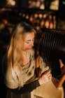 Романтична чарівна жінка з світлим волоссям насолоджується мелодією, граючи на музичному інструменті і сидячи в саду влітку — стокове фото