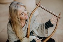 Сверху вдохновила очаровательная женщина с светлыми волосами наслаждаясь музыкой, играя на музыкальном струнном инструменте на террасе — стоковое фото