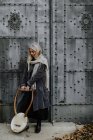 Задумчивая привлекательная блондинка-музыкантка нежно держит струнный музыкальный инструмент, стоя у металлических ворот — стоковое фото