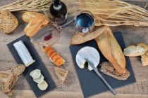 De cima de fatias caseiras saborosas de queijo branco e pão crocante fresco com garrafa e copo de vinho tinto na mesa de madeira rústica — Fotografia de Stock