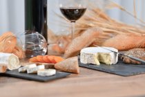 Смачні домашні скибочки білого сиру і свіжий хліб з пляшкою і склянкою червоного вина на сільському дерев'яному столі — стокове фото