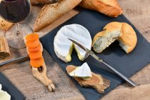 De arriba sabrosos trozos caseros de queso blanco y pan crujiente fresco con botella y copa de vino tinto en la mesa de madera rústica - foto de stock
