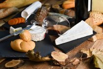 Leckere hausgemachte Scheiben Weißkäse und frisches, knuspriges Brot mit Flasche und Glas Rotwein auf rustikalem Holztisch — Stockfoto