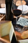 Gustose fette fatte in casa di formaggio bianco e pane fresco croccante con bottiglia e bicchiere di vino rosso su tavolo rustico in legno — Foto stock