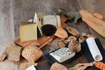 Сверху вкусные домашние ломтики белого сыра и свежий хрустящий хлеб с бутылкой и бокалом красного вина на деревенском деревянном столе — стоковое фото