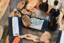 Сверху вкусные домашние ломтики белого сыра и свежий хрустящий хлеб с бутылкой и бокалом красного вина на деревенском деревянном столе — стоковое фото