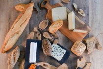 D'en haut délicieux différents types de fromage blanc et de pain frais croustillant avec des morceaux de bois sur la table rustique — Photo de stock