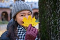 Женщина в теплой одежде смотрит в камеру и закрывает лицо желтым картонным листочком, стоя в норвежском городе Осло — стоковое фото