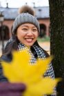Asiatische Frau in warmer Kleidung, die in die Kamera blickt und ihr Gesicht mit gelbem Ahornblatt bedeckt, während sie in der Osloer Kathedrale in Norwegen steht — Stockfoto
