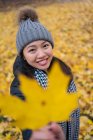 Весела дівчина з Азії, яка кидає жовте листя кленового дерева, стоячи на подвір 