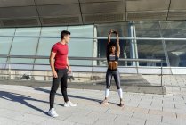 Athletic man giving support to active African American woman in performing of stretching exercise during workout — Stock Photo