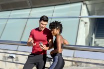 Personal Trainer mit Smartphone und zeigt einer lächelnden Afroamerikanerin App, während sie neben dem Gebäude zusammen steht — Stockfoto