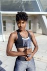 Mulher afro-americana em esportes no topo de pé ao lado da construção e exploração de garrafa de água, enquanto tem pausa durante o treinamento — Fotografia de Stock