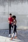 Homem caucasiano alegre com garrafa de água e Africano mulher americana compartilhando smartphone de pé juntos — Fotografia de Stock