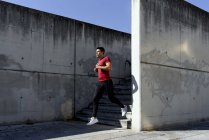 Man in red shirt and black pants running down stairs during workout in sunny summer day in city — Stock Photo