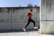 Homem em camisa vermelha e calças pretas correndo para baixo escadas durante o treino no dia de verão ensolarado na cidade — Fotografia de Stock