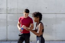 Веселый мужчина с бутылкой воды и афроамериканка делят смартфон стоя — стоковое фото