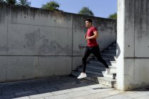 Man in red shirt and black pants running down stairs during workout in sunny summer day in city — Stock Photo