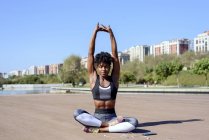 Donna afroamericana in top sportivo e leggings seduti in posa di loto e allungando le mani mentre si rilassa — Foto stock
