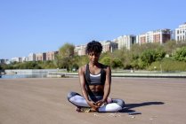 Афроамериканка в спортивном топе и ногах, сидящая в позе лотоса и растягивающая руки вверх, расслабляясь — стоковое фото
