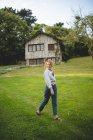 Vista laterale di casuale calma giovane donna godendo passeggiata sul prato verde vicino a casa in legno nel villaggio rurale nelle Asturie, Spagna — Foto stock