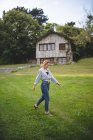 Vista lateral de la tranquila y casual joven mujer disfrutando de un paseo por el prado verde cerca de la casa de madera en el pueblo rural de Asturias, España - foto de stock