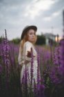 Blurred redhead woman in trendy hat with closed eyes enjoying smell of salvia blossom in meadow of Asturias, Spain — Stock Photo