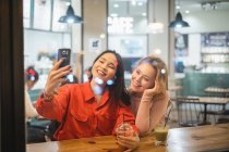 Mujeres jóvenes tomando selfie en la cafetería - foto de stock