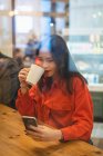 Жінка має чашку кави за допомогою мобільного телефону — стокове фото