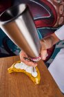 Faceless from above man using cream whipper and piping white fresh cream on banana at table — Stock Photo