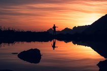 Silhouette of person balancing on shore and reflecting in calm water surrounded by mountains in Switzerland — Stock Photo
