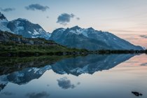Leere Küste des ruhigen Sees in schneebedeckten Bergen, die den Himmel in der Schweiz spiegeln — Stockfoto