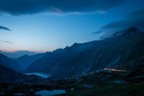 Misteriosa cordillera azul oscuro y río entre pendientes con luces a lo largo de la carretera en Suiza - foto de stock
