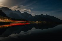 Dramatic breathtaking landscape of red-lit shore and dark tranquil water reflecting cloudy sky and mountains in Switzerland — Stock Photo