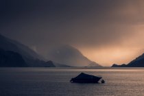 Calm landscape of dark boat in wavy water under gray cloudy sky in mountains in Switzerland — Stock Photo