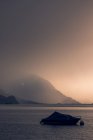 Спокойный пейзаж темной лодки в волнистой воде под серым облачным небом в горах Швейцарии — стоковое фото