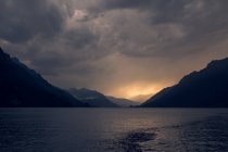 Paisaje tranquilo de aguas oscuras onduladas bajo un cielo gris nublado en las montañas de Suiza - foto de stock