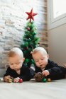 Gemelli sul pavimento vicino all'albero di Natale — Foto stock
