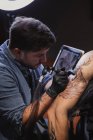 Maître faisant le tatouage sur l'avant-bras du client masculin — Photo de stock