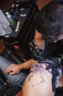 Maestro haciendo tatuaje en el antebrazo del cliente masculino - foto de stock