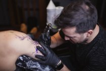 Maestro haciendo tatuaje en el antebrazo del cliente masculino - foto de stock