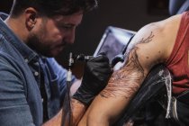 Master facendo tatuaggio sull'avambraccio del cliente maschile — Foto stock