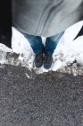 Top view of person in jeans and trekking shoes standing on asphalt snowy road at daytime — Stock Photo