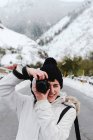 Donna in giacca bianca invernale con cappuccio e pantaloni neri scattare foto con macchina fotografica mentre in piedi in mezzo alla strada asfaltata — Foto stock