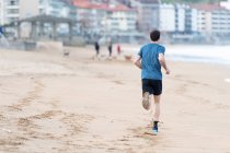 Back view of Sportsman in active wear jogging on lonely beach — Stock Photo