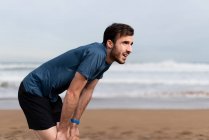 Вид сбоку босоногого спортивного мужчины в активной одежде, делающего перерыв после долгого пробега по песчаному пустырю и отводящего взгляд — стоковое фото