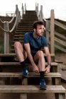 Ginasta macho barbudo em roupas esportivas sentado em escadas de madeira enquanto se prepara para o treino e olhando para longe — Fotografia de Stock