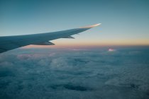 Vista aérea da janela do avião da asa sobre as nuvens no céu bonito da noite com luz do por do sol — Fotografia de Stock