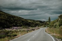Leere, gewundene Asphaltstraße durch grüne Hügel in Neuseeland mit bewölktem, stürmischem Himmel im Hintergrund — Stockfoto